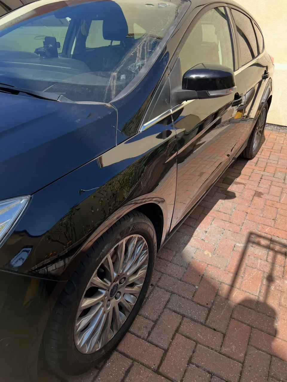Dark car bodywork reflecting the surrounding driveway